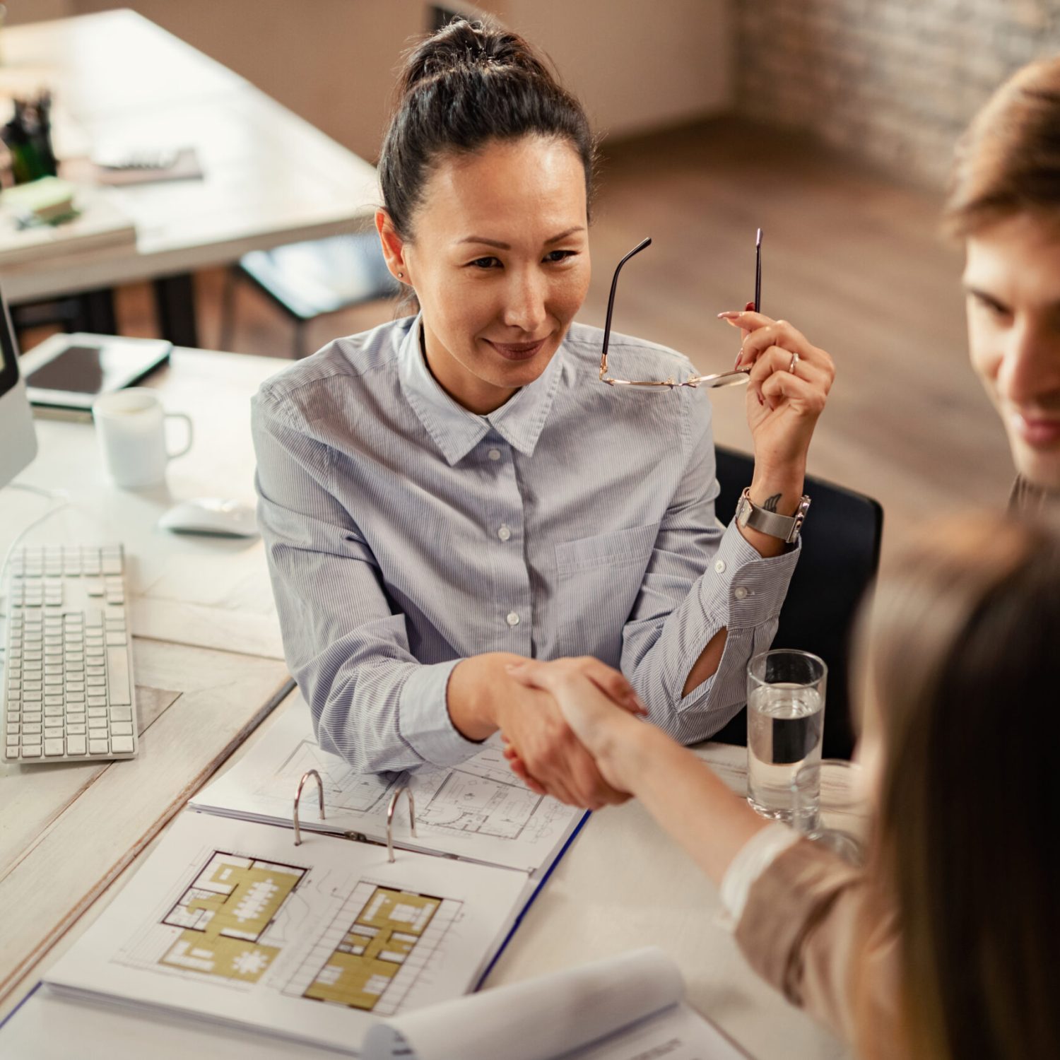 High angle view of Asian financial advisor handshaking with her clients on a meeting in the office.