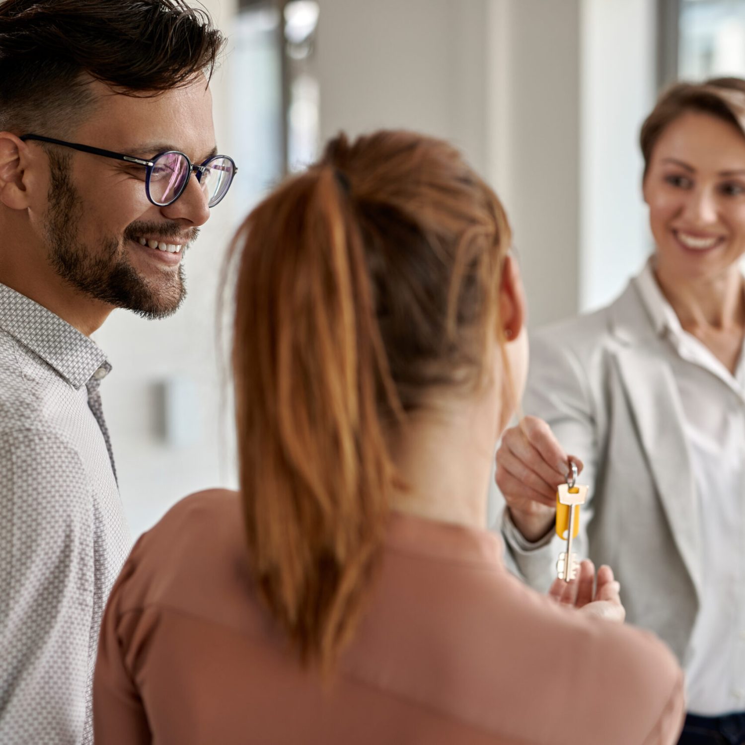 Young happy couple buying a new home and receiving key from their real estate agent.